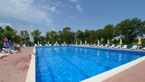 A rectangular swimming pool with clear blue water, surrounded by white lounge chairs and yellow umbrellas. - Villaggio le Palatine (Bernalda)