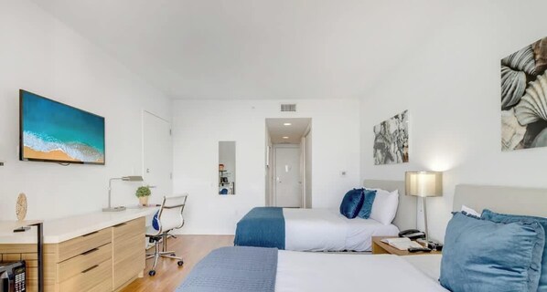 A modern hotel room with a bed, desk, chair, and artwork.