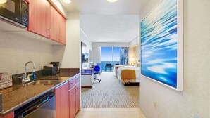 Ein Hotelzimmer mit Küchenzeile, einem Bett, einem Schreibtisch und einem großen Fenster.