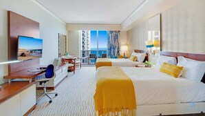 Ein Hotelzimmer mit Schreibtisch, zwei Betten, Fernseher und einem Balkon mit Blick.