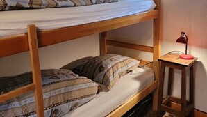 Habitació amb literes, roba de llit amb dibuixos, una taula petita amb una làmpada i una finestra amb cortina.