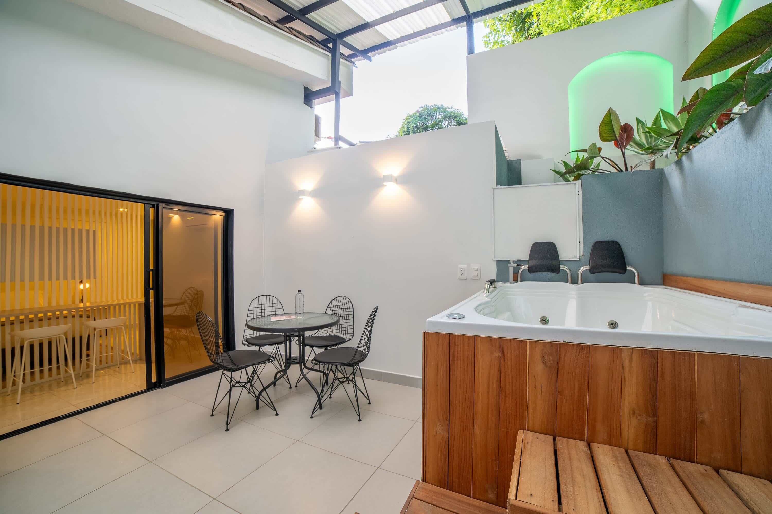 Eine moderne Außenpatio mit Whirlpool, Esstisch mit Stühlen und Glastrennwand, die den Essbereich vom Rest des Raumes abteilt.