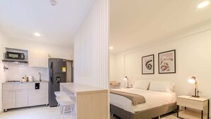 Ett modernt hotellrum med ett litet pentry, en säng med sänggavel, sängbord och konstverk på väggen.