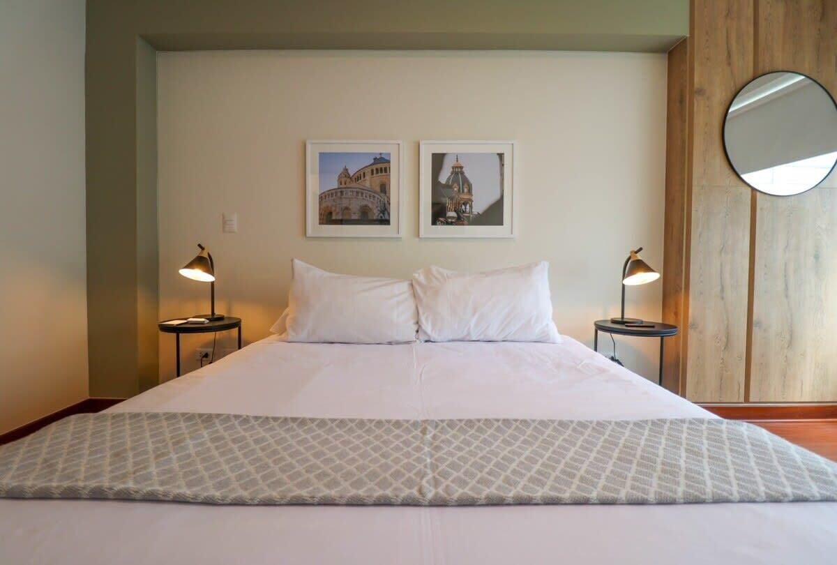 A hotel room with a large bed, two bedside tables with lamps, a round mirror on the wall, and two framed pictures above the bed.