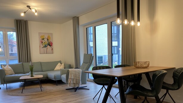 A modern living room with a sofa, a coffee table, a dining table with chairs, and large windows. - Dahmer Dünen - Ostseezauber! (Dahme)