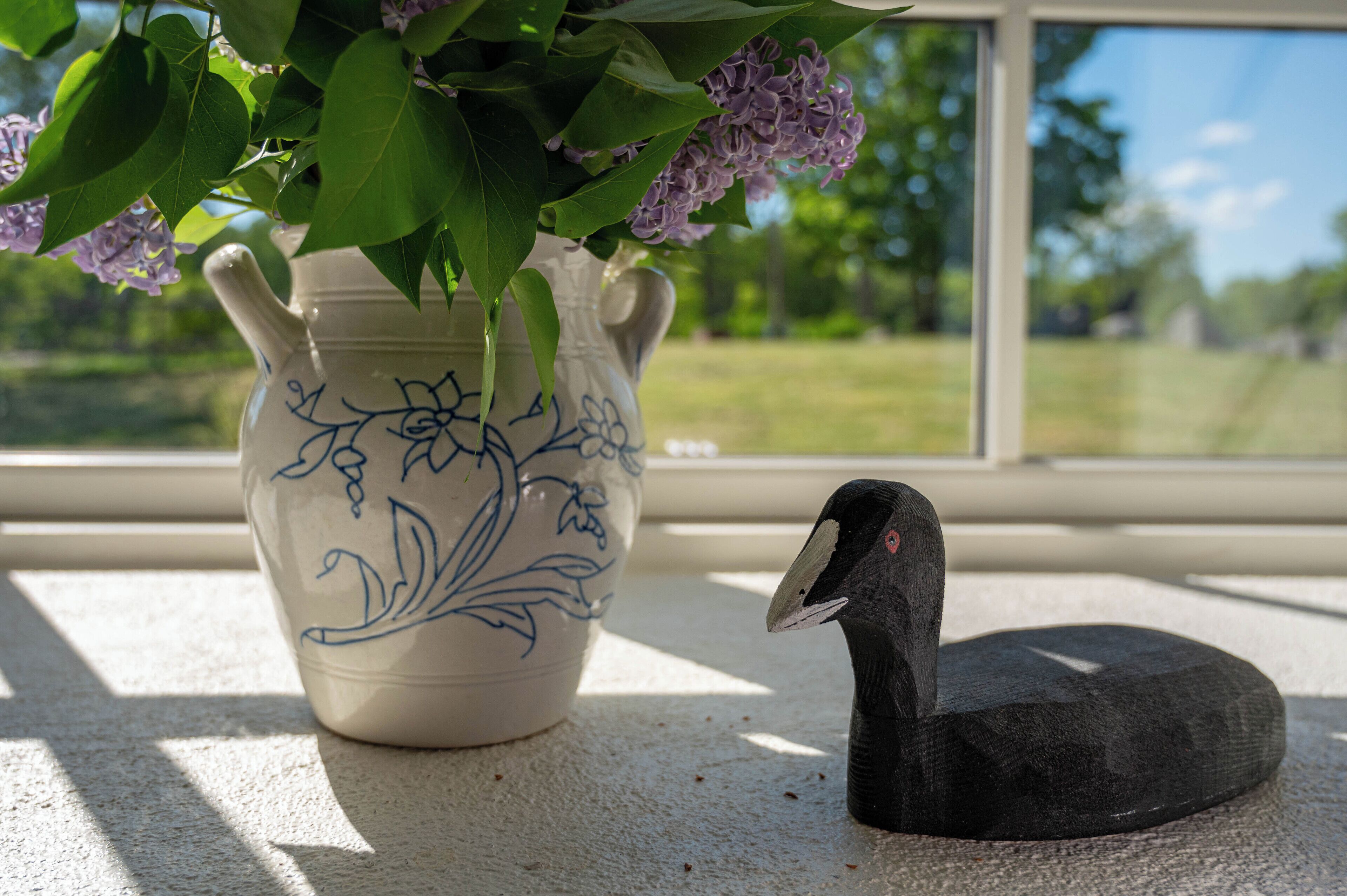 Un jarrón de cerámica con diseños florales y una escultura de pájaro negro en un alféizar.