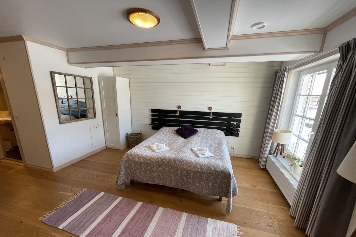 A bedroom with a bed, a window, a lamp, and a wooden floor.