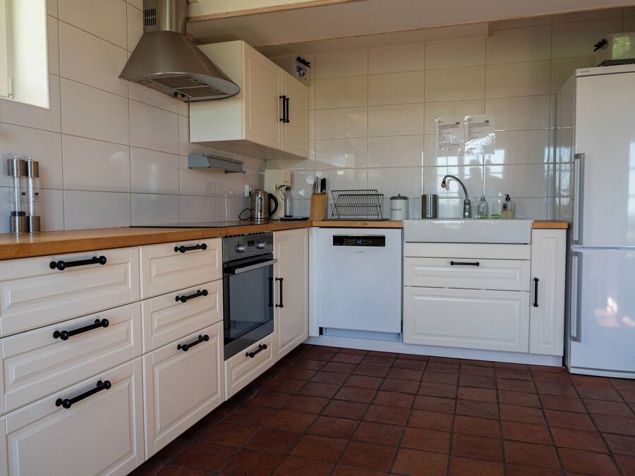 A kitchen with white cabinets, a wooden countertop, a stainless steel range hood, a refrigerator, and a tiled floor.