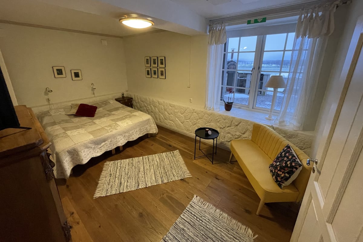 A bedroom with a bed, a sofa, a small table, and a window with a view.