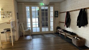 A hotel lobby with a wooden floor, a reception desk, a chair, a coat rack, and a shoe rack. - Låsta Gårdshotell (Strängnäs)
