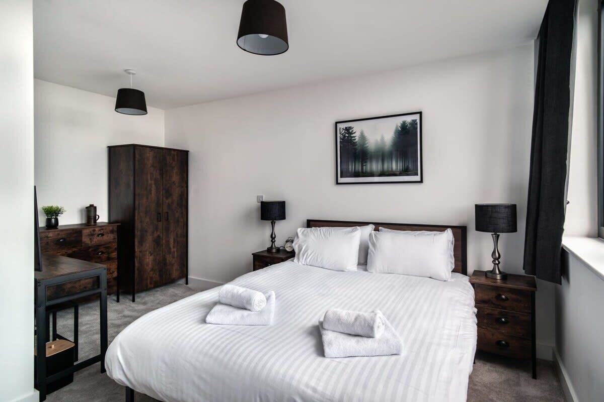 Ein modernes Schlafzimmer mit einem großen Bett, zwei Nachttischen, einem Kleiderschrank und einem gerahmten Bild von einem Wald an der Wand.