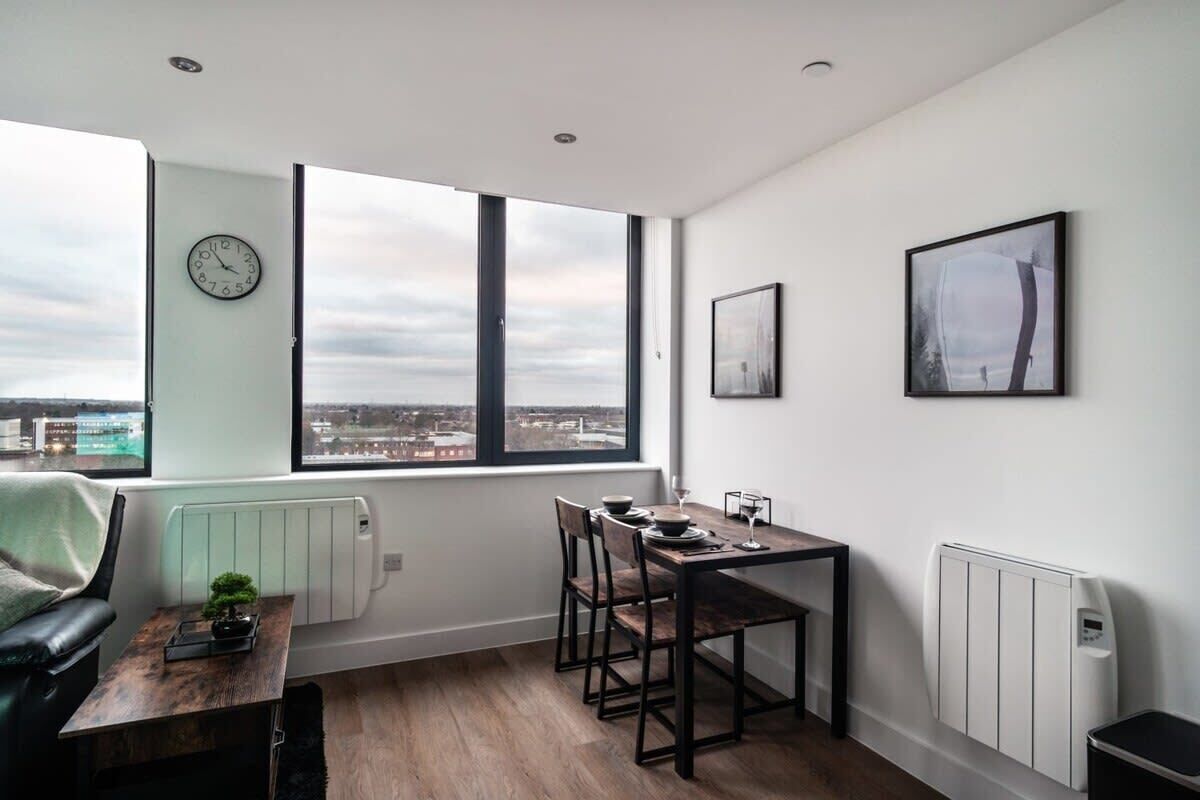 A modern room with a dining table, chairs, a clock, and a window with a city view.
