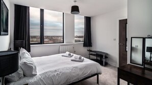 Una habitación de hotel moderna con una cama grande, un escritorio y vistas a la ciudad a través de amplios ventanales.
