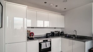 Una cocina moderna con gabinetes blancos, horno empotrado, lavamanos y cafetera.