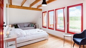 Un dormitorio con cama, sofá, sillón y ventanas amplias con marcos rojos.