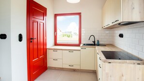 Una cocina con puerta roja, armarios blancos, ventana con vistas y grifo negro.
