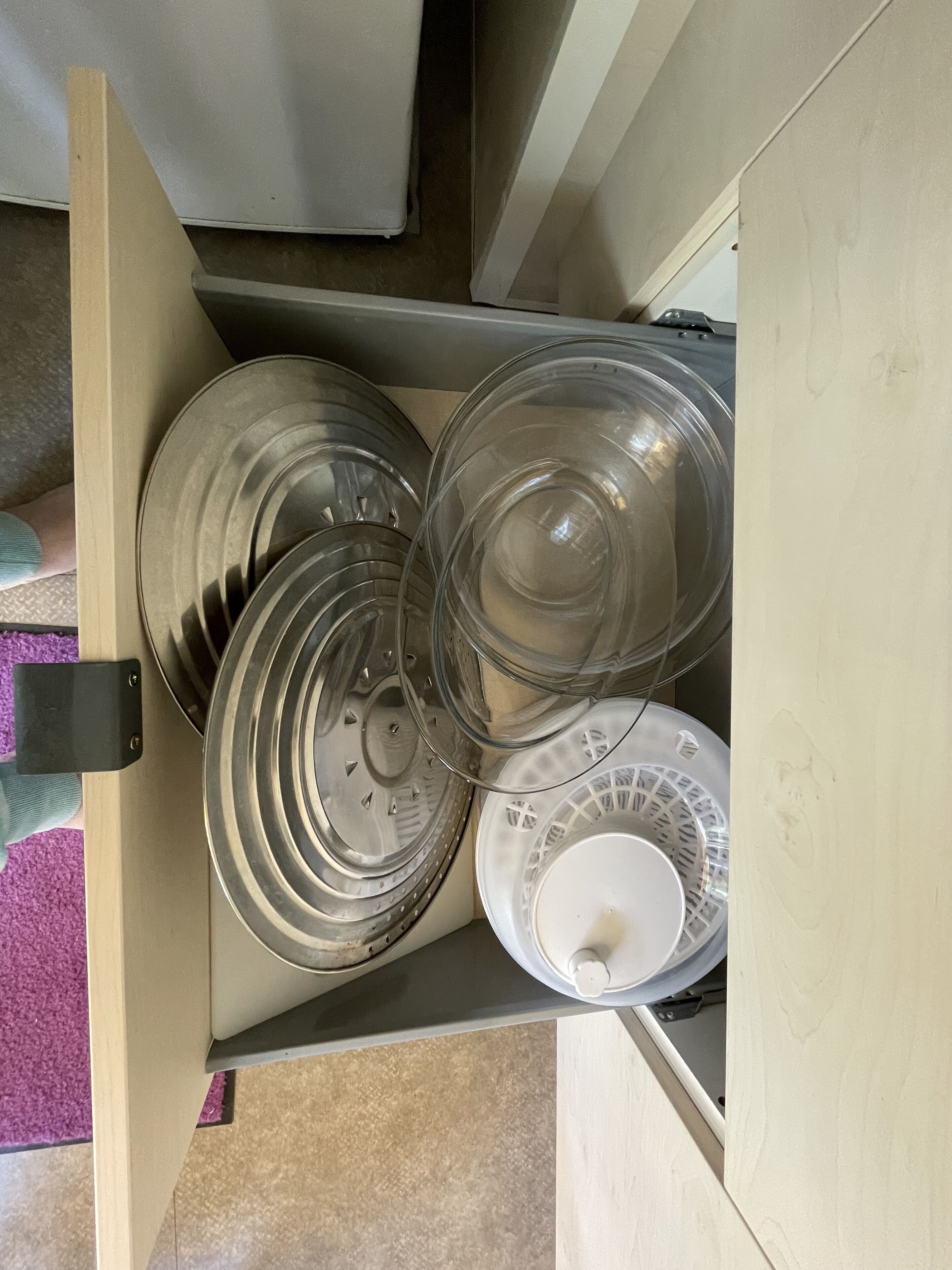 A kitchen drawer with various dishes and a white cup.