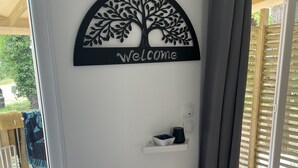 Una habitación con un cartel que dice 'Welcome', un estante pequeño con objetos, y un perro sentado junto a la puerta.