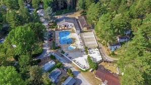 Vista aérea de un complejo turístico con piscina, aparcamiento y varias edificaciones rodeadas de árboles.