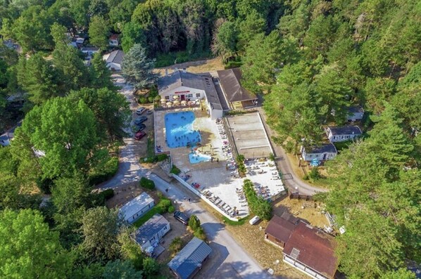 An aerial view of a resort with a swimming pool, a parking area, and several buildings surrounded by trees.