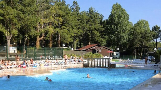 Zona de piscina con varias pistas, rodeada de árboles y un pequeño edificio.