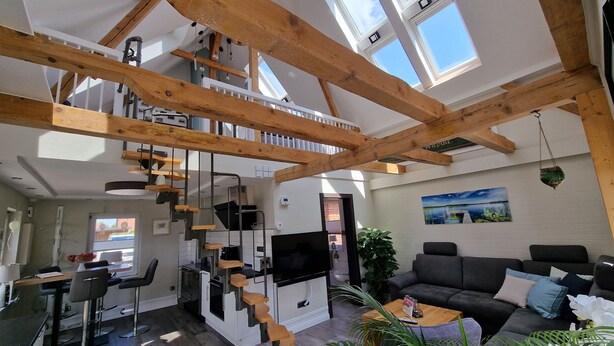 Una cocina moderna con estufa integrada, un comedor con mesa y sillas, una escalera y una sala de estar con sofá y un cuadro en la pared.