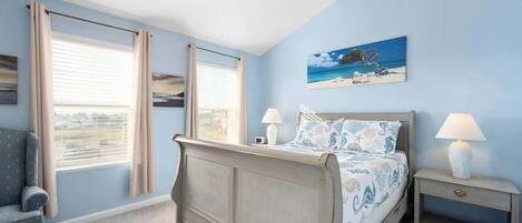 Une chambre à coucher avec un lit, deux tables de chevet, une chaise et une fenêtre avec des rideaux.