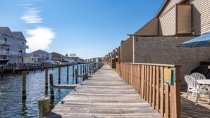 A wooden pier leading to a waterfront property with a row of houses on one side and a stone wall on the other. - Waterfront Ocean Villa! (Ocean City)