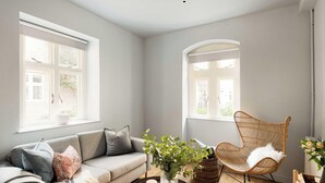 Ein modernes Wohnzimmer mit einem grauen Sofa, einem Korbstuhl und einem großen Fenster, das für natürliches Licht sorgt.