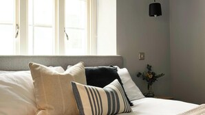A neatly made bed with white and striped pillows, a grey headboard, and a black pendant light. - King Apartment · Courtyard Garden in Bath (Bath and North East Somerset)