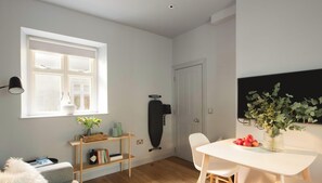 Een moderne, goed verlichte kamer met een groot raam, een loopfiets, een witte tafel met een schaal fruit en een potplant.