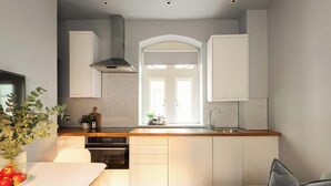 A modern kitchen with a central island, a built-in oven, and a window with a view. - King Apartment · Courtyard Garden in Bath (Bath and North East Somerset)