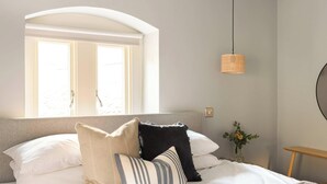 Een slaapkamer met een bed, een raam, een hanglamp en een tafeltje met een bloevas.