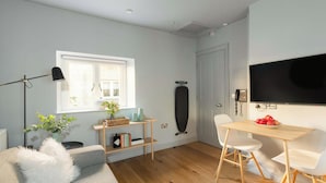 A modern living room with a wooden floor, a grey sofa, a coffee table, a TV, and a bookshelf with books and decorative items. - Cosy King Apartment · Central Bath (Bath and North East Somerset)