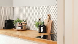 Una encimera de cocina con una cafetera, una botella de aceite de oliva, una tabla de cortar y una planta.