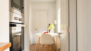 A compact kitchen with a white door, a dining table with a chair, and a vase with flowers. - King Suite for 4 · Courtyard Views in Bath (Bath and North East Somerset)