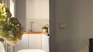 A modern kitchen with a white countertop, a hexagonal backsplash, and a sink. There is a bowl of red apples on a white chair. - King Suite for 4 · Courtyard Views in Bath (Bath and North East Somerset)