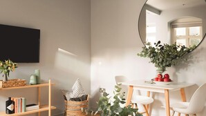 A modern dining area with a white table, chairs, and a mirror reflecting a window. There are baskets on shelves, a vase with flowers, and a bottle on the table. - Elegant King Suite · Behind Thermae Spa (Bath and North East Somerset)