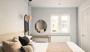 A bedroom with a bed, bedside table, mirror, and window. - St Catherine's Hospital - Deluxe Apartment (Bath and North East Somerset)