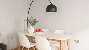 A modern dining area with a round table, four white chairs, a vase with green leaves, and a bowl of red apples. - Open-Plan Suite for 4 · Steps from Roman Baths (Bath and North East Somerset)