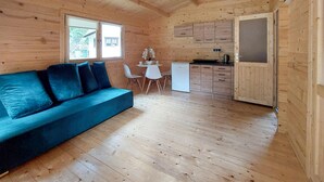 L’intérieur d’un chalet en bois, avec un canapé bleu, une table à manger et des chaises, un petit coin cuisine et une fenêtre.