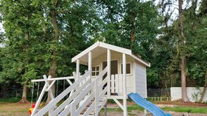 Une cabane en bois avec un toboggan et des escaliers, entourée d’arbres.