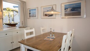 Uma área de refeições com uma mesa de madeira, cadeiras brancas e quadros nas paredes.