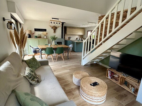 A modern living room with a sofa, dining table, and chairs. A staircase leads to an upper level.