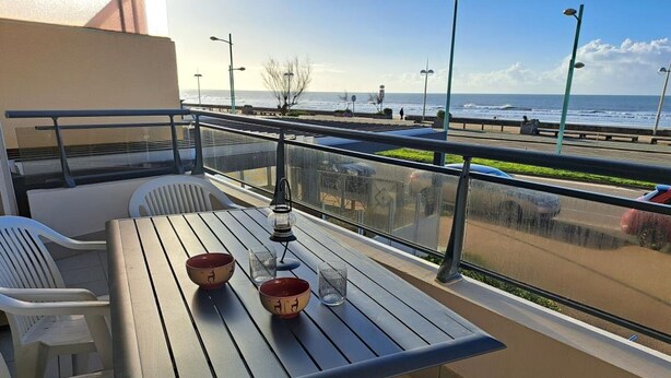 A balcony with a table, chairs, and a view of the beach and ocean.