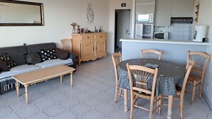 A compact living space with a sofa, a dining table with chairs, a kitchen area with a microwave, and a hanging light fixture.
