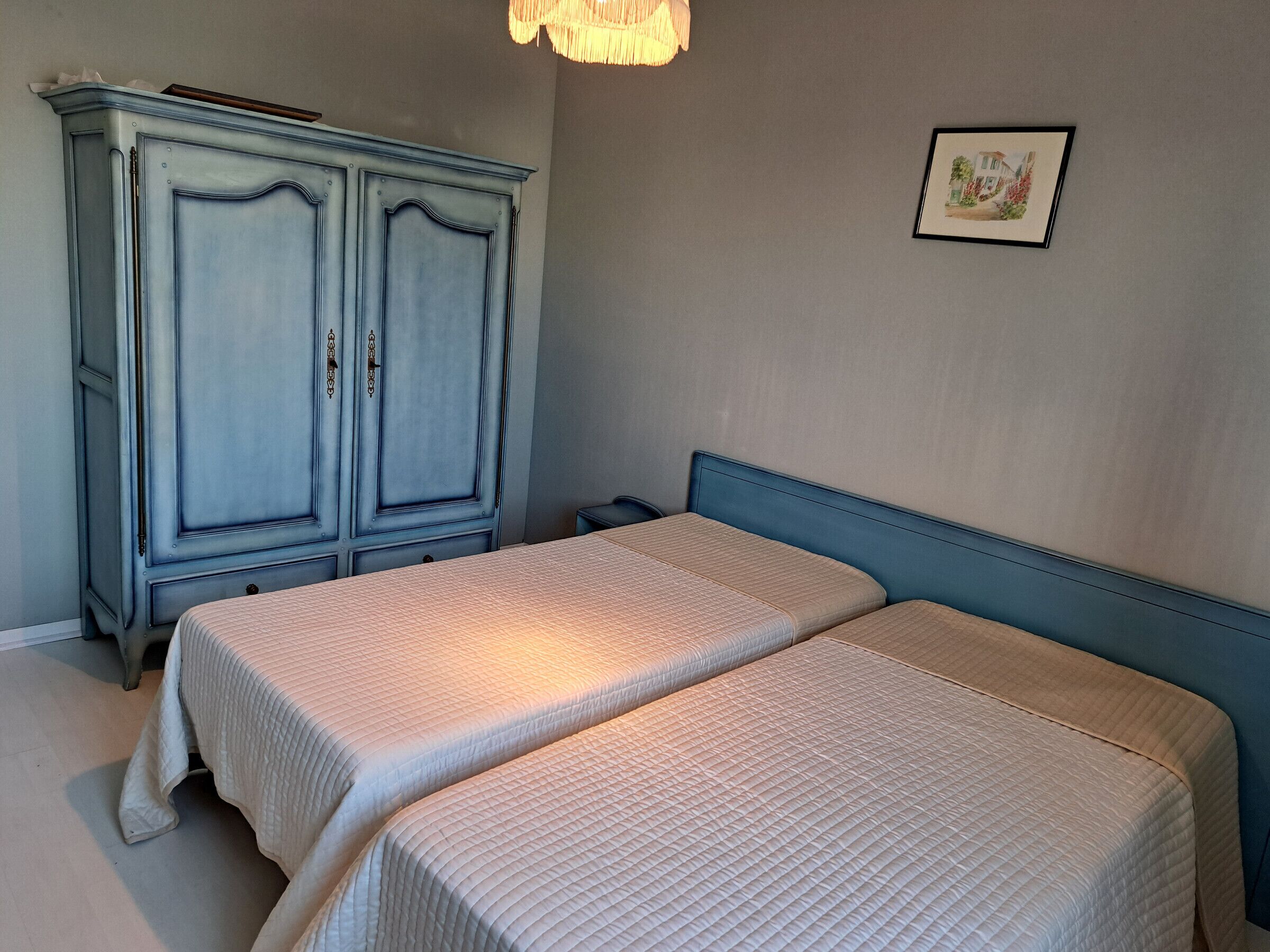 Ein Schlafzimmer mit zwei Betten, einem Kleiderschrank und einem gerahmten Bild an der Wand.