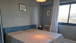 A hotel room with two beds, a chair, a nightstand, and a window with a view.