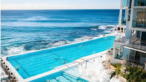 A large outdoor swimming pool with clear blue water, adjacent to a rocky coastline and the ocean.