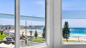 A view from a window overlooking a beach and ocean, with a clear sky and a road in the foreground.